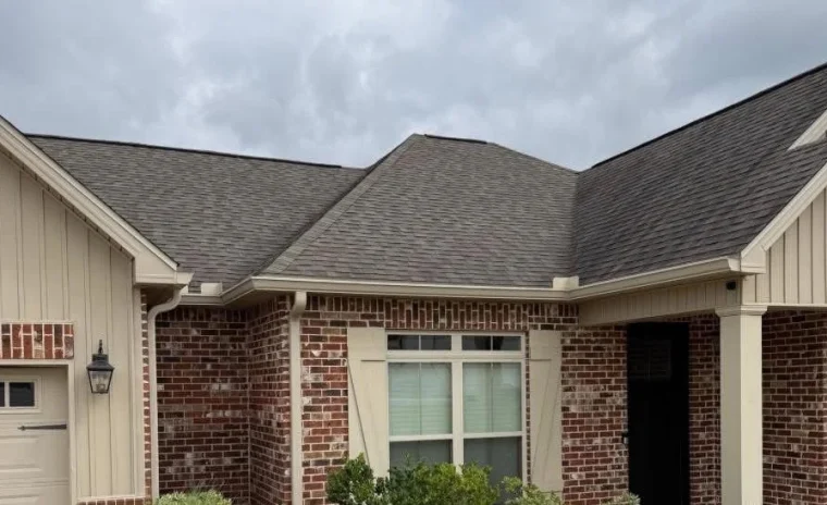 A house with brick and tan siding, brown roof, and new white gutters.