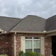 A house with brick and tan siding, brown roof, and new white gutters.